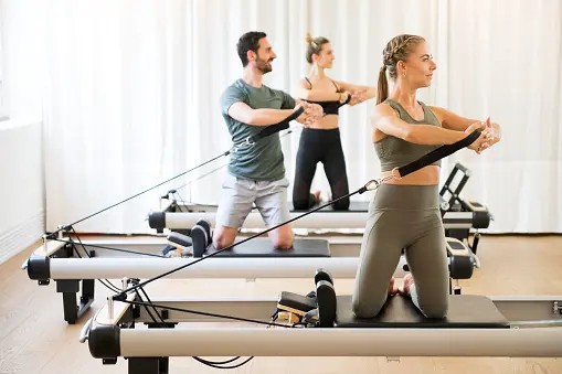 A group of people in gym clothes on some reformer machines
